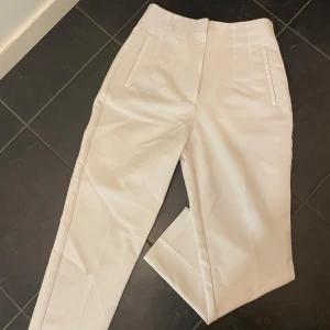 Vita kostymbyxor - Säljer ett par stilrena vita kostymbyxor i mycket bra skick. De är högmidjade med en elegant straight passform. Byxorna har diskreta fickor (trådarna på ena fickan är uppsprättade, går att sprätta upp den andra för att använda fickorna)