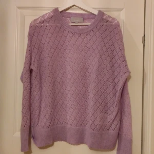 Ljuslila stickad tröja från InWear - Säljer en ljuslila stickad tröja från InWear med ett fint hålmönster. Tröjan har långa ärmar och ribbade kanter vid ärmslut och nederkant. Perfekt för en mysig dag!