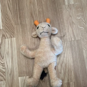 Mjukisdjur i form av en giraff - Säljer ett gulligt mjukisdjur som föreställer en giraff. Den är beige med bruna fläckar och har svarta detaljer på manen. Giraffen har orange horn och en liten svans. Perfekt som kramkompis eller dekoration i barnrummet.