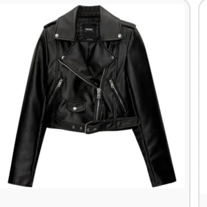Svart skinnjacka - Snygg svart skinnjacka med dragkedjor och knappar. Jackan har en croppad design och bälte i midjan. Från pull & bear