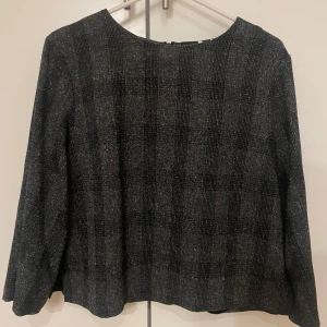 Blus/topp - Säljer en stilren grå tröja från Visual Clothing Project. Tröjan har ett diskret rutmönster och långa ärmar. Perfekt för en elegant och avslappnad look.