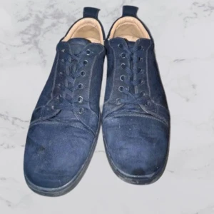 Mörkblå Louboutin  - Snygga mörkblå sneakers i mocka med en unik röd sula. Skorna har snörning och en stilren design som passar perfekt för en avslappnad look. Har dock skada vid foten på ena skon därför ett billigare pris.