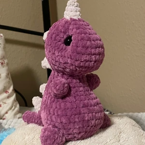 Virkat gosedjur-dinosaurie - perfekt julklapp - Säljer en lila dinosaurie amigurumi som är lite över 20 cm hög, perfekt för både stora och små dinosauriefans! ❤️ Virkad med mjukt chenille-garn av hög kvalitet, fylld med polyester, och försedd med säkerhetsögon.  Finns för avhämtning i Malmö eller kan skickas mot fraktkostnad.  Hör av dig om du vill veta mer eller ge den sin ägare!🦖💚