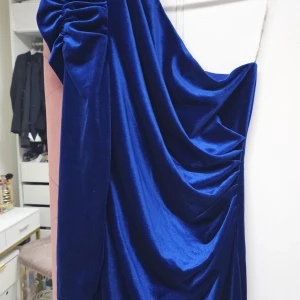 Blå sammetsklänning - Elegant blå sammetsklänning med en one-shoulder design. Klänningen har en draperad stil som ger en lyxig känsla. Perfekt för speciella tillfällen.