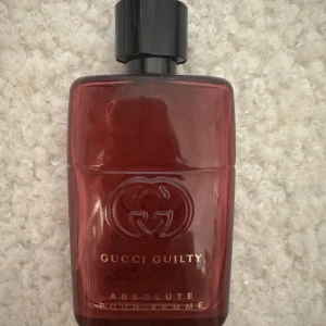Gucci Guilty Absolute Pour Femme parfym - Elegant parfymflaska i djupröd nyans från Gucci. Flaskan är halvfull. Flaskan har en stilren design med svart kork och det ikoniska Gucci-emblemet ingraverat. Doften är en del av Guilty-serien och passar den som söker en sofistikerad och djärv doftupplevelse. 