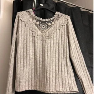 Beige ribbad tröja med spetsdetaljer - Säljer en stilren beige ribbad tröja med vackra spetsdetaljer vid halsringningen. Tröjan har långa ärmar och en elegant design som passar perfekt för både vardag och speciella tillfällen.