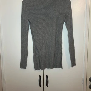 Grå ribbad polotröja från Shein - Säljer en stilren grå ribbad polotröja från Shein. Tröjan har en klassisk design med långa ärmar och en bekväm passform. Perfekt för kyligare dagar. Har slits på båda sidorna