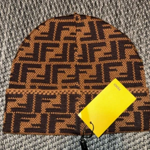 Brun och svart mössa från Fendi - Snygg mössa från Fendi i brunt och svart med ett distinkt mönster. Tillverkad i bomull och perfekt för att hålla dig varm med stil. Ett måste för modeälskare!
