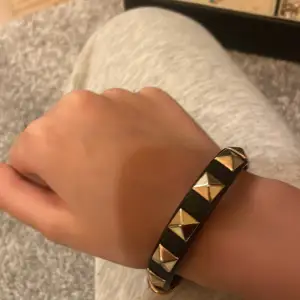 Snyggt svart armband med guldiga nitar som ger en cool look. Perfekt för att piffa upp vilken outfit som helst. Armbandet har ett justerbart spänne för bästa passform. Passar både till vardags och fest!