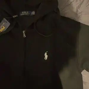 Säljer en snygg svart hoodie från Polo Ralph Lauren. Den har en dragkedja framtill och den klassiska loggan broderad på bröstet. Perfekt för både vardag och chill. Storleken är L men passar XS. Hör av dig vid intresse!