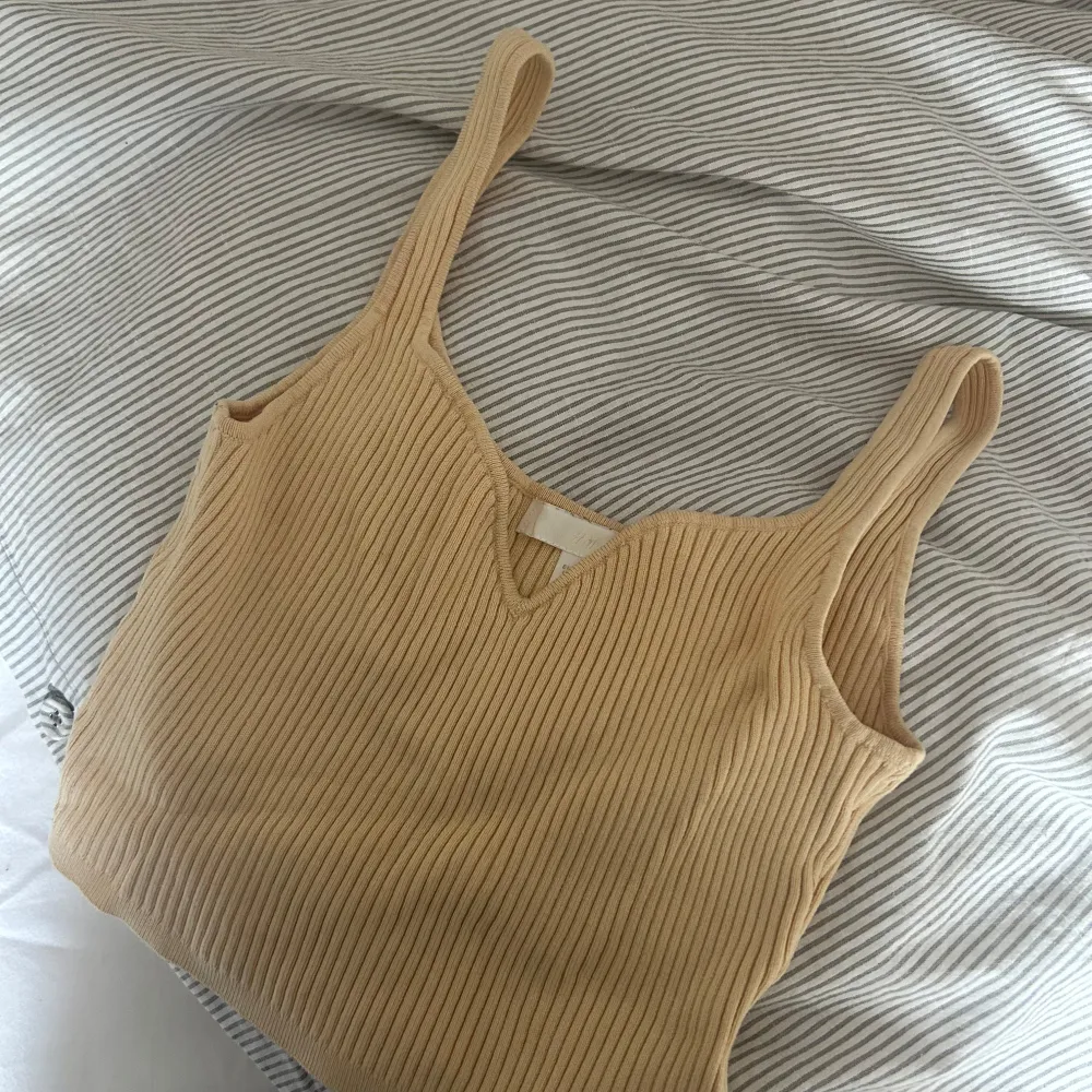 Säljer en superfin gul ribbad linnetopp i mycket bra skick. Toppen har en v-ringad design och är perfekt för sommardagar. Den är ärmlös och har en skön passform som passar till både vardag och fest. Perfekt att matcha med jeans eller kjol!. Yläosat.