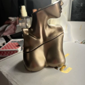 Eilish parfym av Billie Eilish - Säljer en unik och sensuell parfym från Billie Eilish. Flaskan är formad som en byst i guld, inspirerad av halsen, nyckelbenen och bröstet. Doften har krämiga vaniljnoter, mjuka kryddor och kakao, med en bas av tonkaböna och varma mysknoter. Cruelty free och vegansk. Perfekt för både dag och kväll! 50ml använd sparsamt så mycket kvar! Tyvärr har förbacking blivit lite skadad (se bild) men inget som skadar funktionen 