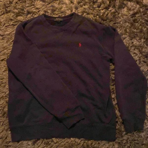 Mörkblå tröja från Polo Ralph Lauren - Säljer en snygg mörkblå tröja från Polo Ralph Lauren i storlek XL i barnstorlek vilket motsvarar S. Den har en klassisk design med ett rött broderat märke på bröstet. Perfekt för både vardag och lite finare tillfällen. Tröjan är i bra skick och redo för en ny ägare!