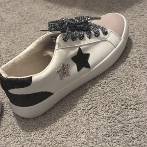 Vita sneakers med stjärndetaljer - Snygga vita sneakers med coola stjärndetaljer i svart och silver. Skorna har leopardmönstrade snören och en svart detalj vid hälen. Perfekta för att ge din outfit en unik touch! 🖤✨Storlek 36-37