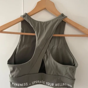 Grå sporttopp från Pureness - Snygg och bekväm grå sporttopp från Pureness. Perfekt för träning med sitt stretchiga material och stilrena design. Toppen har en brottarrygg och elastisk kant med texten 'UPGRADE YOUR WELLBEING'.
