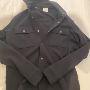Svart overshirt från Selected Homme - Säljer en stilren svart overshirt från Selected Homme i mycket bra skick.       Är inte använd, eftersom att den är lite för stor för mig.      Köpte den nypris 799 kr.          Mitt pris: 500.       Det är storlek S