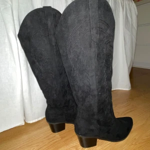 Svarta cowboy boots i mocka - Snygga svarta cowboy boots i mocka med snygga detaljer. De har en rejäl klack och spetsig tå, perfekta för countryfesten eller utgång.                                       Klacken är 5cm