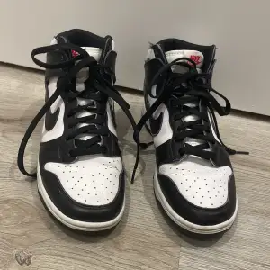 Säljer ett par klassiska Nike panda dunks. Skorna har en snygg hög design med snörning och den ikoniska Nike-loggan på sidan. Perfekta för både vardag och fest! De är i bra skick med lite slitage på sulorna. Passar perfekt för dig som älskar streetwear och sneakers.