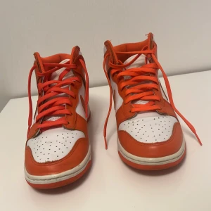 Orange och vita Nike sneakers - Säljer ett par snygga Nike sneakers i orange och vitt. De har en klassisk hög modell med snörning och är i bra skick. Perfekta för både vardag och träning. Storleken är US 7,5 vilket motsvarar ungefär dam 38 eller herr 40,41. Skorna har en cool retrostil som verkligen sticker ut! ÄKTA diskuteras priser.