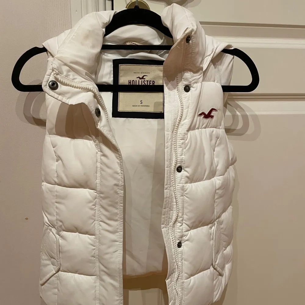 Säljer en snygg vit dunväst från Hollister i storlek S. Västen har en mysig huva och stängs med dragkedja och knappar. Perfekt för kyliga dagar och ger en stilren look. Passar bra till både vardag och fest! Strl S men liten i storleken . Takit.