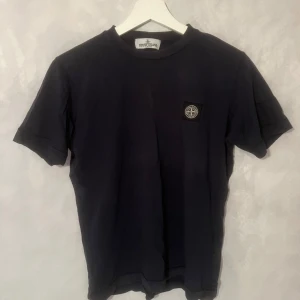 Mörkblå  t-shirt från Stone Island Junior - Säljer en snygg svart t-shirt från Stone Island Junior. På bröstet finns det ikoniska Stone Island-märket. Har ett minimalt hål i nacken. 