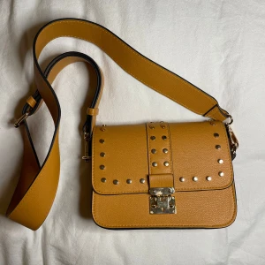 Axelväska med nitar - Säljer denna gul/bruna väskan från Lindex med nitar på framsidan.