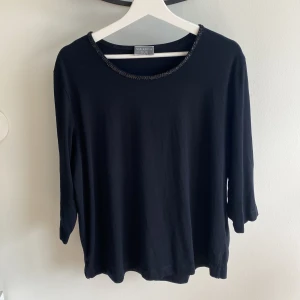 Svart tröja med paljetter - Svart tröja med 3/4-ärmar och svarta paljetter på halsringningen. Fint skick, har själv aldrig använt den men är inköpt på second hand. Oklart vilken storlek då det inte går att hitta på plagget, men skulle gissa på L/XL.  93% bomull och 7% elastan. 