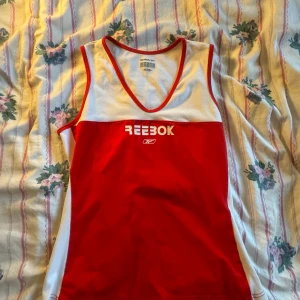  linnetopp från Reebok - Säljer en sportig och bekväm röd och vit linnetopp från Reebok. Toppen är ärmlös och har en klassisk Reebok-logga på framsidan. Perfekt för träning eller en varm sommardag. Den är i bra skick och redo för nya äventyr! Den var min mammas i 2010 men senare har hon inte fått användning av den och tror toppen säljs inte längre. Pris kan diskuteras💗💗🎀