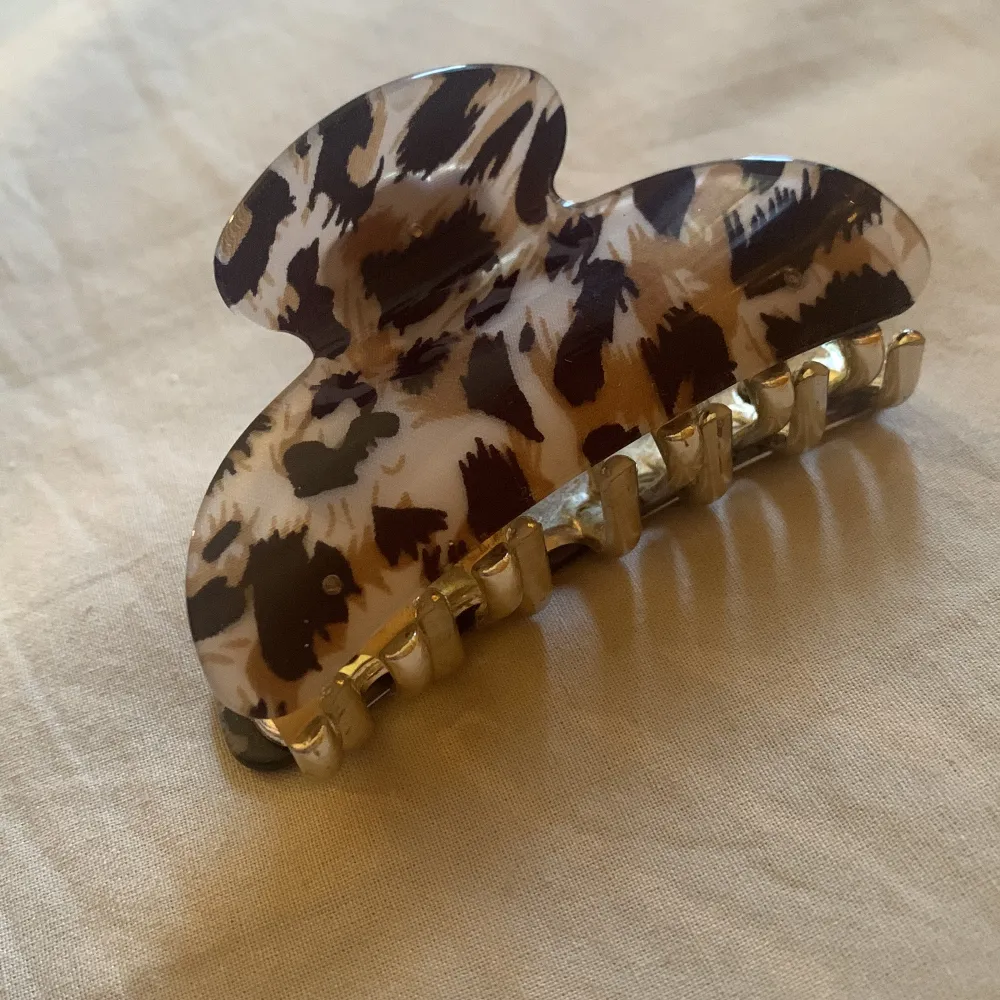 Säljer en fin hårklämma med leopardmönster. Den har en snygg mix av bruna, svarta och beige färger som verkligen poppar. Klämman är i plast och har en guldig metallmekanism som håller håret på plats. Perfekt för att ge din look lite extra edge! 🐆✨. Accessoarer.