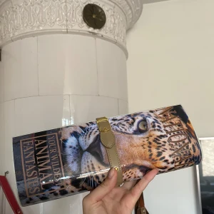 Kuvertväska med leopardmönster - Säljer en supercool kuvertväska med ett djärvt leopardmönster. Väskan har en glansig yta och stängs med en snygg rem med magnet. Perfekt för att ge din outfit en vild touch! 🐆💓