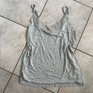 Grå linnetopp från Gina Tricot - Säljer en söt grå linnetopp från Gina Tricot. Den har spetsdetaljer vid halsringningen och en liten rosett framtill. Perfekt för sommardagar eller som ett lager under en kofta. Toppen är i ett mjukt och bekvämt material. skriv vid frågor💗