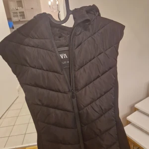 Svart dunväst från Zara - Säljer en snygg och varm svart dunväst från Zara. Perfekt för höst och vinter med en praktisk dragkedja framtill. Västen har en quiltad design och är i nyskick. Perfekt för lager-på-lager-stil!