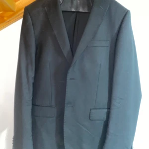 Svart kavaj från Dressmann - Säljer en elegant svart kavaj från Dressmann i storlek 48. Den är tillverkad av 100% ull vilket ger en lyxig känsla och perfekt passform. Kavajen har en klassisk design med två knappar framtill och är i nyskick. Perfekt för både formella tillfällen och fest.                               byxor I storlek 31-32 följer med. 