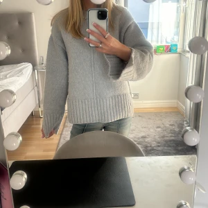 Grå stickad tröja - Säljer en supermysig grå stickad tröja som är perfekt för kyliga dagar. Den har en lös passform och långa ärmar, vilket gör den både bekväm och stilren. Tröjan har en bred ribbad kant vid ärmslut och nederkant som ger en snygg detalj. Perfekt att matcha med jeans för en avslappnad look!