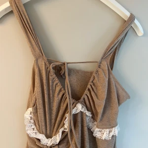 Beige klänning med spetsdetaljer - Säljer en superfin beige klänning med vackra spetsdetaljer. Klänningen har en snygg omlott-design och knytning i ryggen. Den är ärmlös och har en volangdetalj framtill.