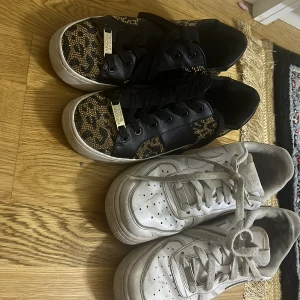 Två par sneakers till salu - Säljer två par sneakers. Det första paret är svarta med glittriga leopardmönster och snörning, perfekt för en festlig look. Det andra paret är vita Nike Air Force, klassiska och bekväma för vardagsbruk. Säljer båda för 1000kr