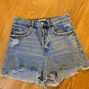 Blå jeansshorts från H&M - Säljer ett par snygga blå Mid waist jeansshorts från H&M i storlek XS. De har en cool distressed look med slitna detaljer och fransiga kanter. Ny skick!!