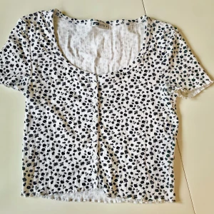 Vit blommig topp från F21 - Söt vit topp med små svarta blommor från F21. Den har korta ärmar och en rundad halsringning. Perfekt för en avslappnad sommarlook!