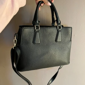 Svart handväska  - Svart väska i jättebra skick! Stor nog för dator och har dessutom olika fack. Fint material som hållt bra, inga sprickor eller yttre defekter :) !Obs! Det finns ett hål inuti väskan (ej synligt) på tyget men det ej svårt att sy ihop