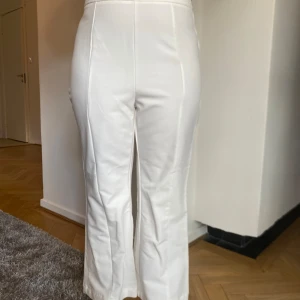 Vita högmidjade byxor - Säljer ett par stilrena vita bootcutbyxor med hög midja. De har en rak passform och är perfekta för både vardag och fest. Byxorna är gjorda i ett mjukt och bekvämt material som ger en snygg siluett.