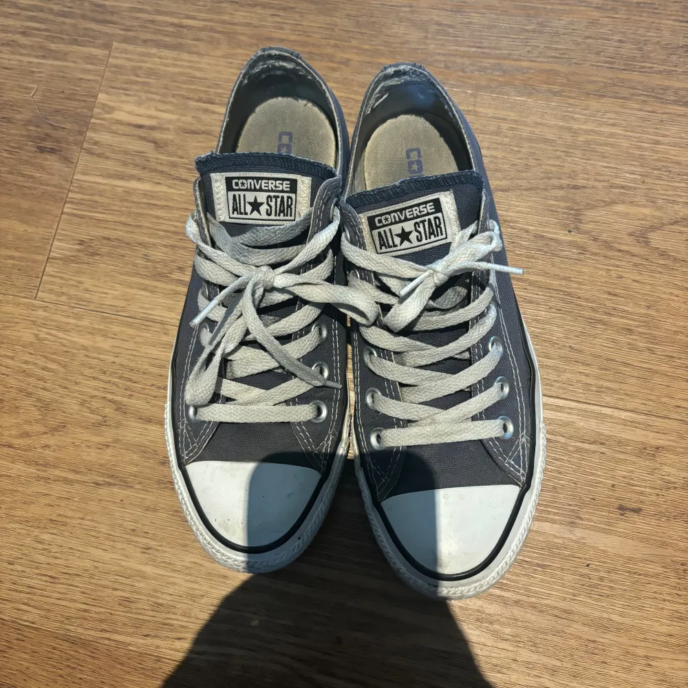 Säljer ett par klassiska svarta Converse All Star sneakers. De har en vit tåhätta och vita snören. Skorna är i använt skick med lite slitage på insidan, men de är fortfarande superbekväma och perfekta för vardagsbruk.. Skor.