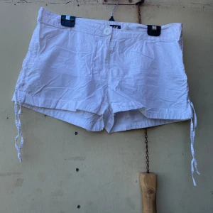 Vita shorts från H&M - Säljer ett par vita shorts från H&M. De är i en lätt och bekväm bomullskvalitet, perfekta för varma sommardagar. Shortsen har en knapp och dragkedja framtill samt knytband i sidorna för en justerbar passform. De har också två bakfickor för en avslappnad stil.