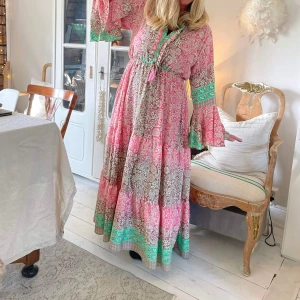 Love Forever Färgglad långklänning - Säljer en superfin långklänning med ett färgglatt mönster i rosa, grönt och beige. Klänningen har långa, vida ärmar och knytning under bysten. Perfekt för sommarens fester eller utlandsresan. Hämtas på Hägerstensåsen eller ök. 