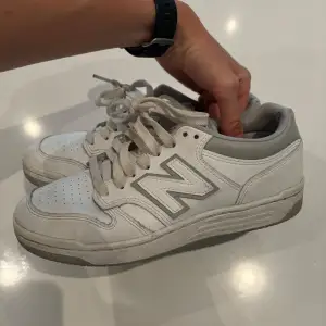 Säljer ett par vita sneakers från New Balance. De har en klassisk design med snörning och det ikoniska 'N' på sidan. Skorna är i syntetmaterial och har en bekväm passform. Perfekta för vardagsbruk!