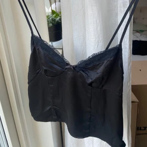 Svart satinlinne från H&M - Säljer ett elegant svart satinlinne från H&M. Det har tunna axelband och en fin spetsdetalj vid urringningen. Perfekt för en utekväll eller att bära under en kavaj för en chic look.