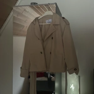 Beige trenchcoat från Stradivarius - Säljer en snygg beige trenchcoat från Stradivarius i storlek XS. Jackan har klassiska detaljer som knappar och ett bälte i midjan. Använd ett fåtal gånger, så den är i mycket bra skick.