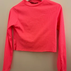 Neonrosa ribbad tröja från Parisian - Säljer en supercool neonrosa ribbad tröja från Parisian. Den är långärmad och har en croppad passform som är perfekt för både vardag och fest. Materialet är mjukt och stretchigt, vilket gör den bekväm att bära hela dagen. Perfekt för att lysa upp din garderob! 💖