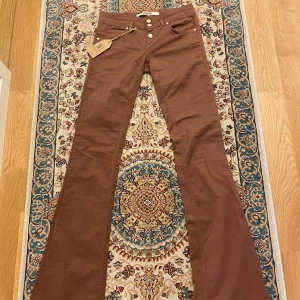 Bruna lowwaisted bootcut byxor från Twenty Easy🤎🥥 💕💗💓 - Säljer ett par snygga bruna bootcut byxor från Twenty Easy. De är lågmidjade med tre knappar fram och har en stjärndetalj på bakfickan. Perfekta för höst och vår , och de ger en riktigt cool retrovibe. Byxorna är i nytt skick med etikett kvar. Passar perfekt för en avslappnad men stilren look! Säljer eftersom de är för långa för mig. Midjemåttet är 36cm tvärs över 🤎🥥🍂🍁🌺🌸🌼🌟⭐️