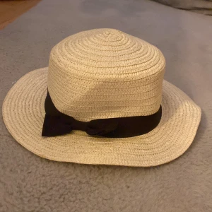 Beige stråhatt med svart band - Snygg beige stråhatt perfekt för sommardagar! Den har ett brett svart band med en söt rosett som detalj. Hatten är i mycket bra skick och passar perfekt för en dag på stranden eller en sommarfest. Ett måste för att hålla solen borta med stil! 🏖️inte änvänd många gånger .
