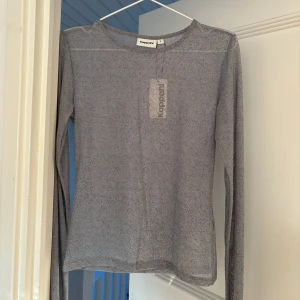 Grå glittrig topp från Kappahl - Säljer en superfin grå glittrig topp från Kappahl i storlek S. Den är perfekt för festliga tillfällen med sitt skimrande material. Toppen har långa ärmar och en normal passform. Ny med prislapp kvar!
